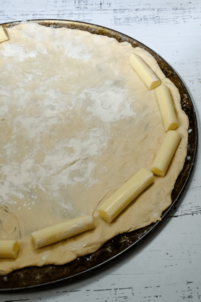 Laying the string cheese around the edge of the pizza dough