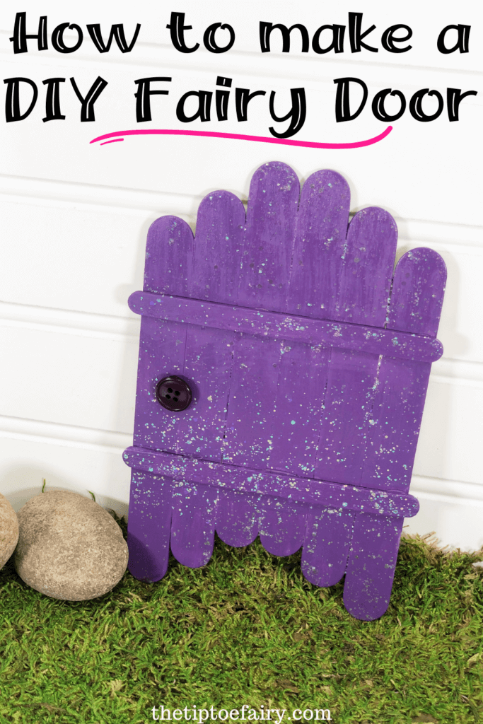 Close up image of the purple diy fairy door on a white shiplap background with green moss underneath the door and rocks to the left. 