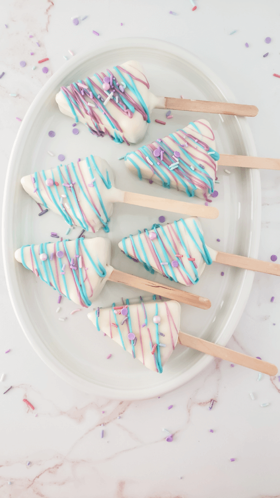 Five slices of Unicorn Cheesecake on a Stick with sprinkles on an oval plate. 