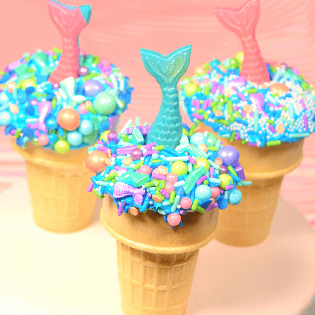 Three mermaid ice cream cone cupcakes ready to eat - two with pink tails and one with a blue tail. 