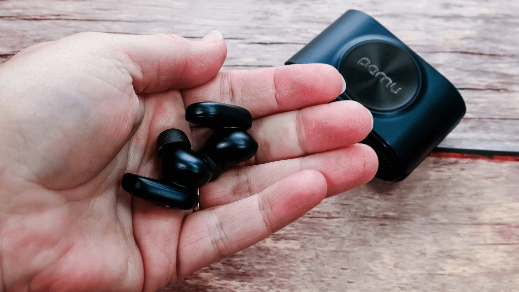 A hand holding the PaMu Slide 2 ANC Wireless Earbuds with the case behind them. 