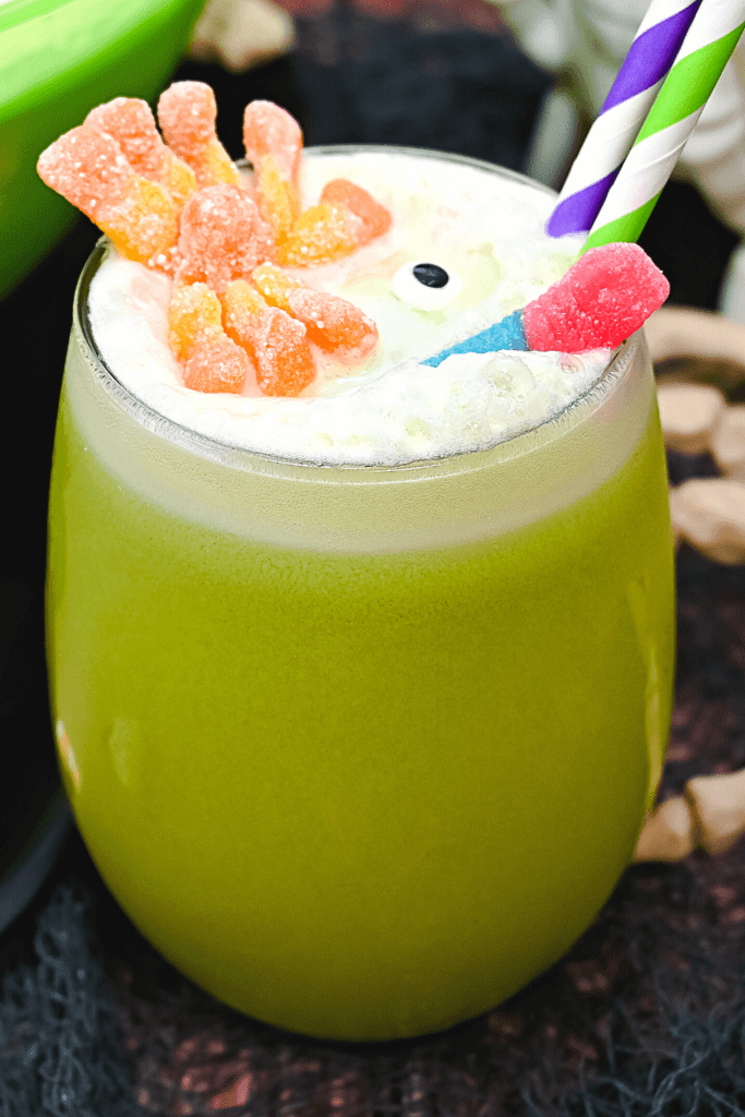 Close up view of one glass of witch's brew halloween punch with the orange spider, red and blue gummy worm, and a candy eye. 