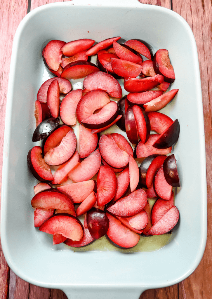 Sliced plums over melted butter in a blue 9 x 13 baking dish. 