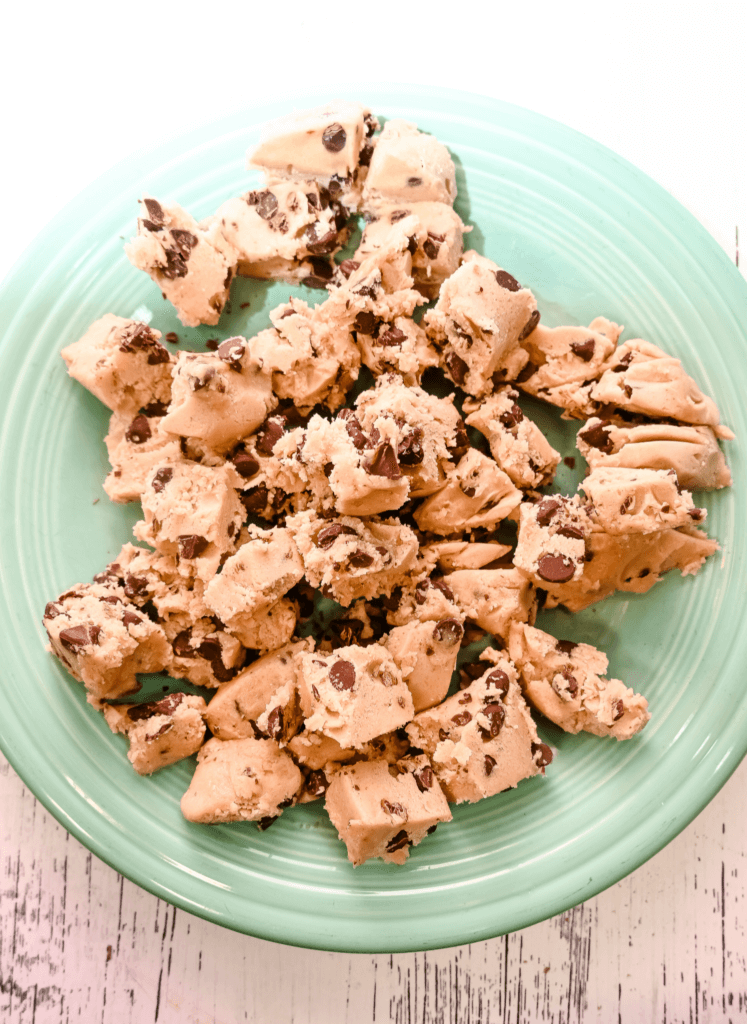 A green plate full of cut up pieces of chocolate chip cookie dough