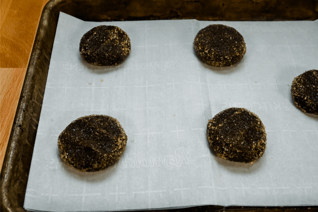 Chocolate cookie dough covered in turbinado sugar flattened on parchment paper. 