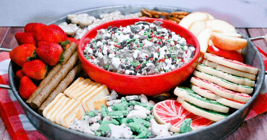 A circular tray full of cookies, fruits, pretzels, and more with Little Debbie's Christmas Tree Cake Dip in the center. 