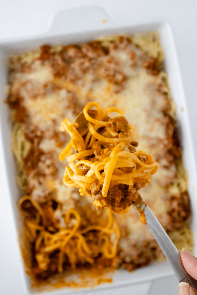 A fork with a bunch of spaghetti alfredo over the casserole dish
