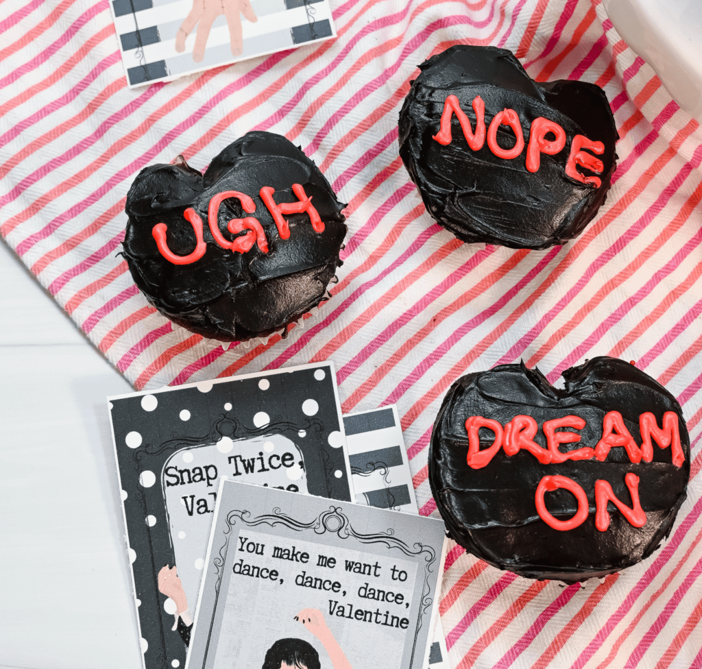 Three finished Anti-Valentine's Day Heart cupcakes with some Wednesday Addams printable valentines