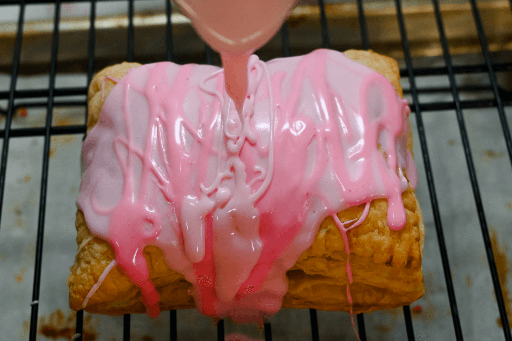 Pouring microwaved pink frosting over the top of the cooled hand pie