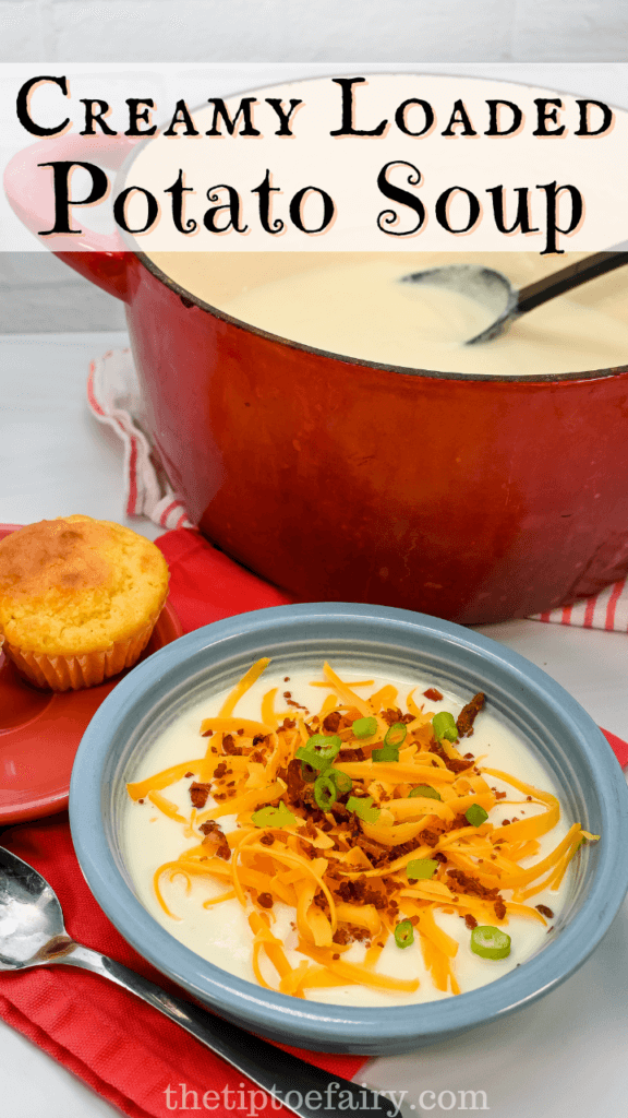 Blue bowl of creamy loaded potato soup next to a cornbread muffin in front of the red pot of soup