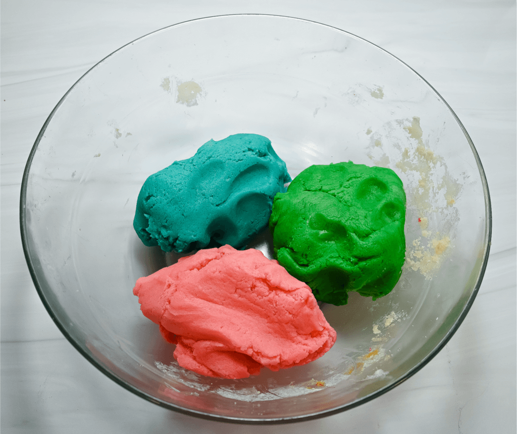 Blue, pink, and green cookie dough in a glass bowl