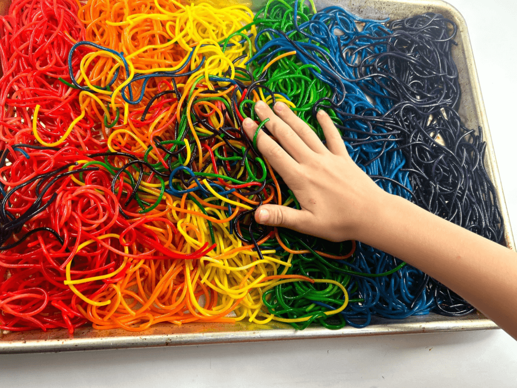 A child's hand mixing up the rainbow spaghetti