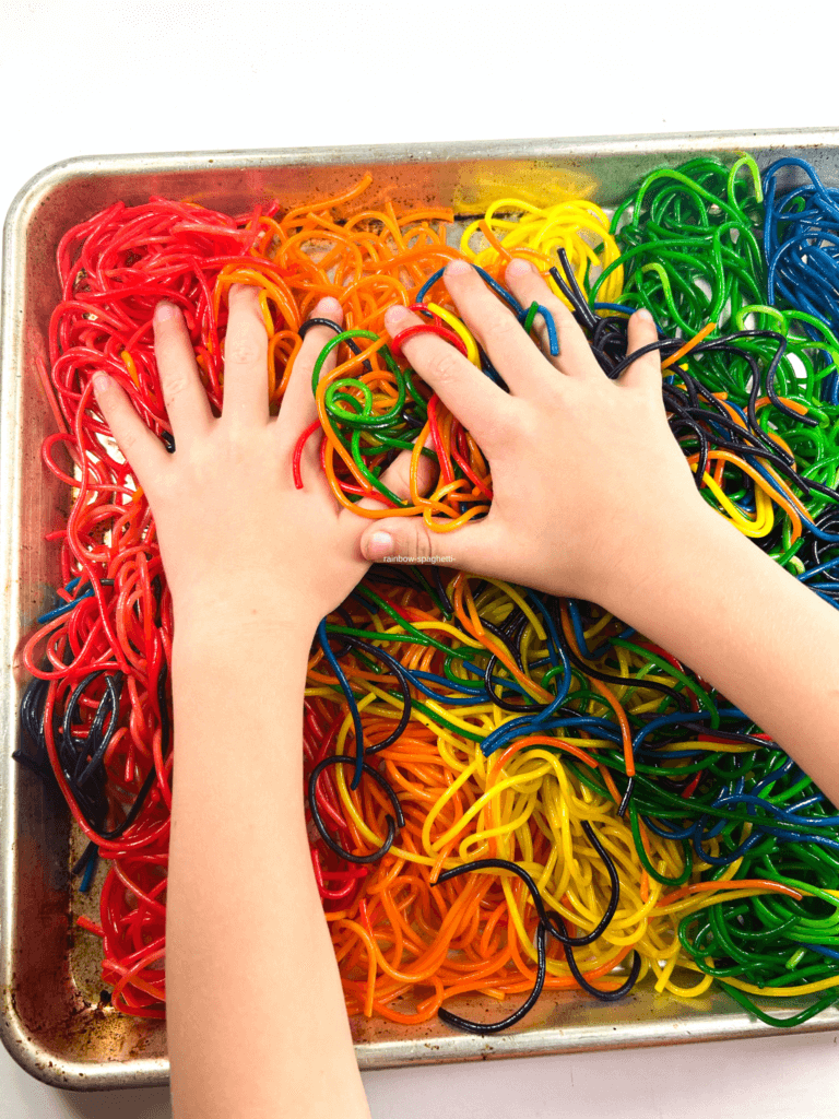 A child's hands in a pan of rainbow spaghetti