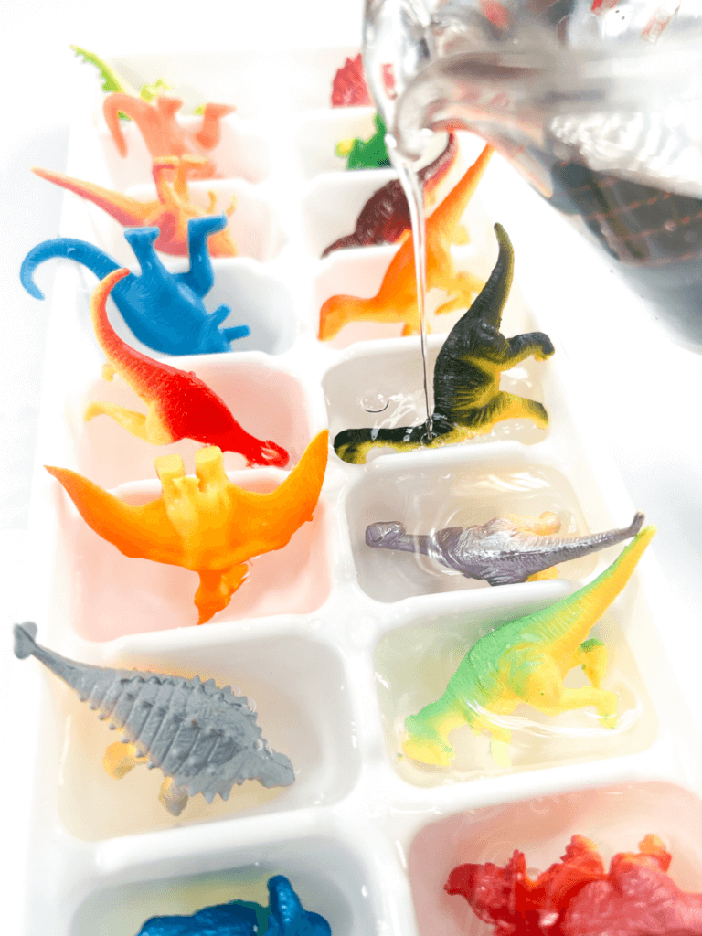 Close up of pouring water into the ice cube trays with dinosaurs