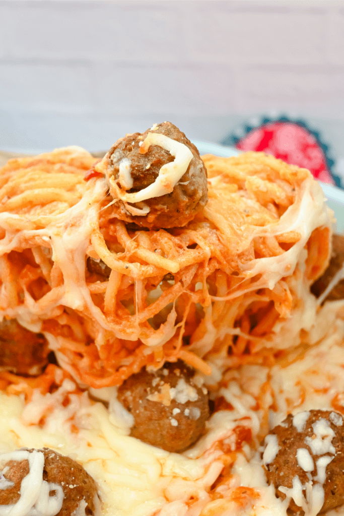 Close up of a big spoonful of spaghetti and meatball casserole with a meatball on top