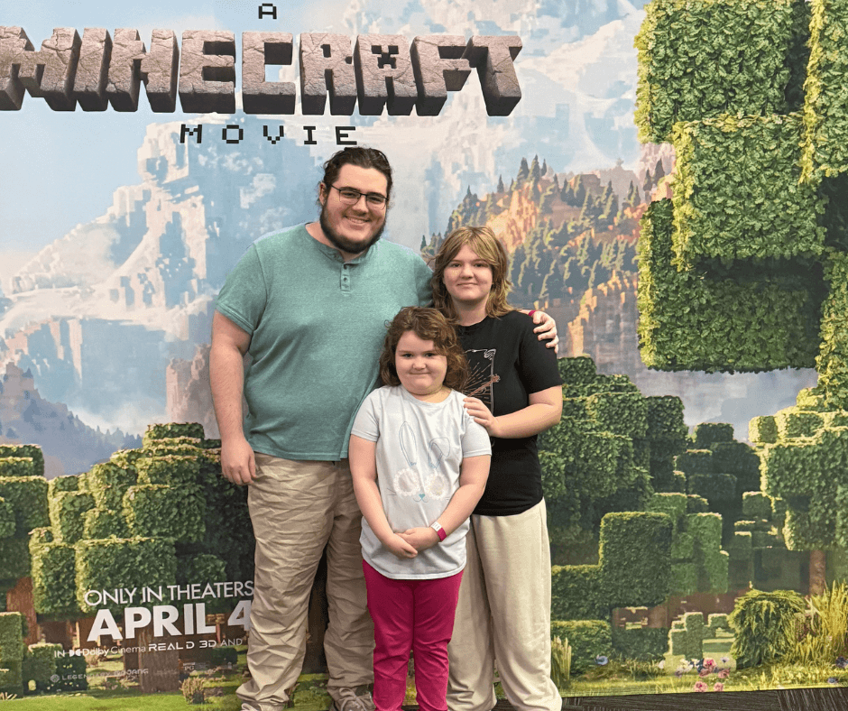 My kids standing in front of the big poster at the movie theater for A Minecraft Movie