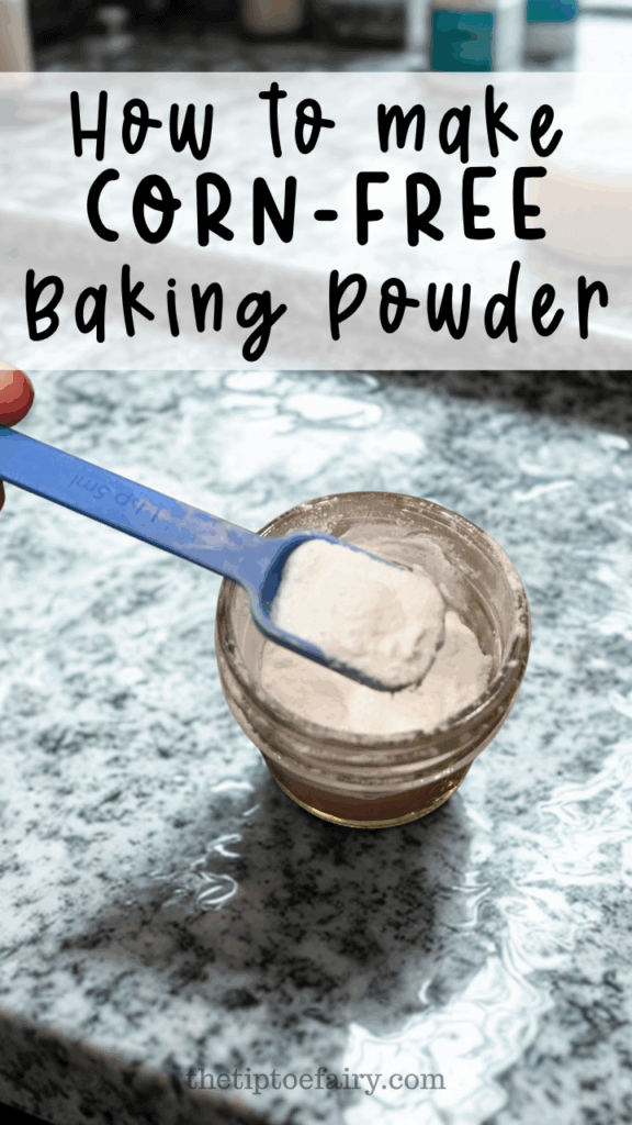 A granite counter top with a glass of corn-free baking powder with a blue spoon over it holding a teaspoons-worth of baking powder.