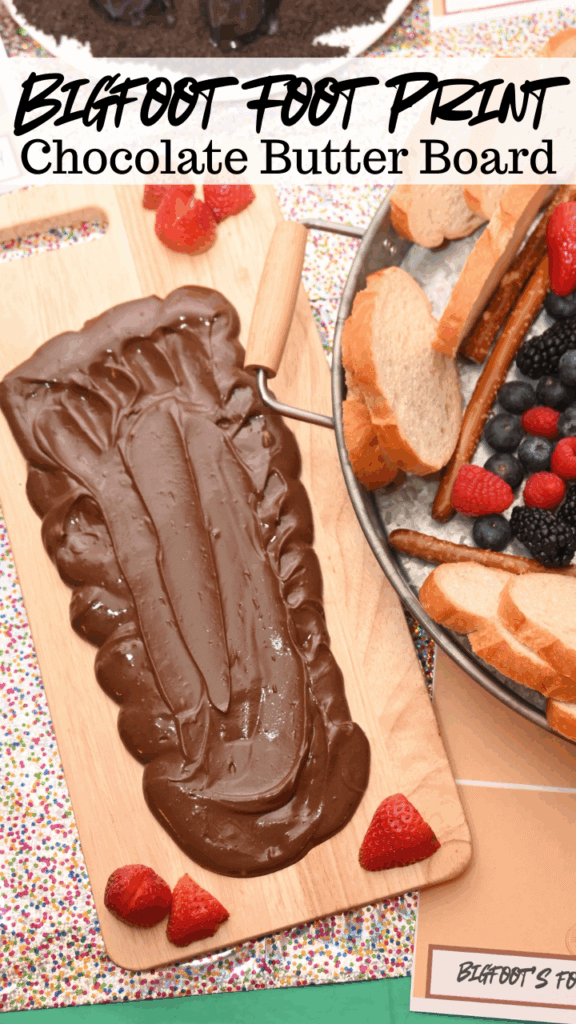 A wooden board with chocolate butter in the shape of a footprint for Bigfoot next to a tray of berries, pretzels, and bread.