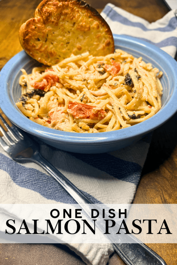 A blue bowl with salmon pasta featuring cherry tomatoes, baby spinach, and fettuccine